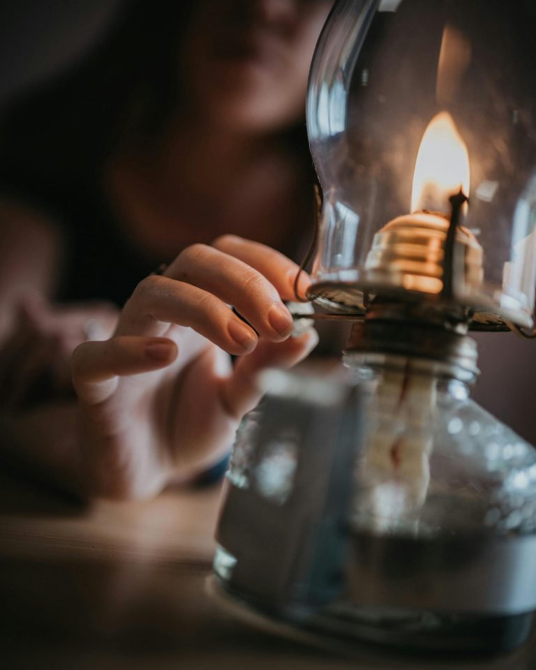 A close-up of a hand reaching for a burning kerosene lamp, creating a warm and intimate ambience.
