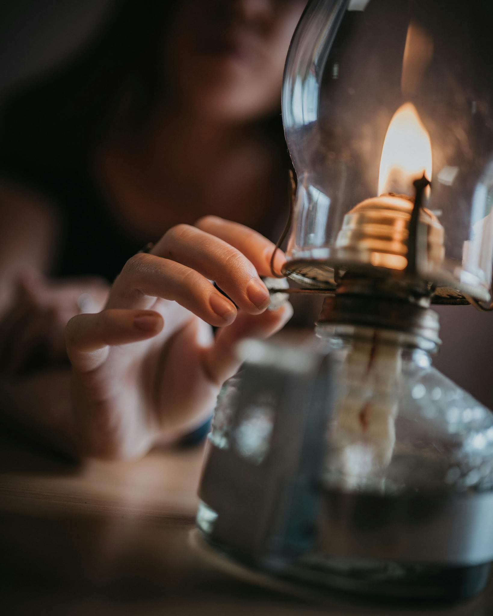 A close-up of a hand reaching for a burning kerosene lamp, creating a warm and intimate ambience.