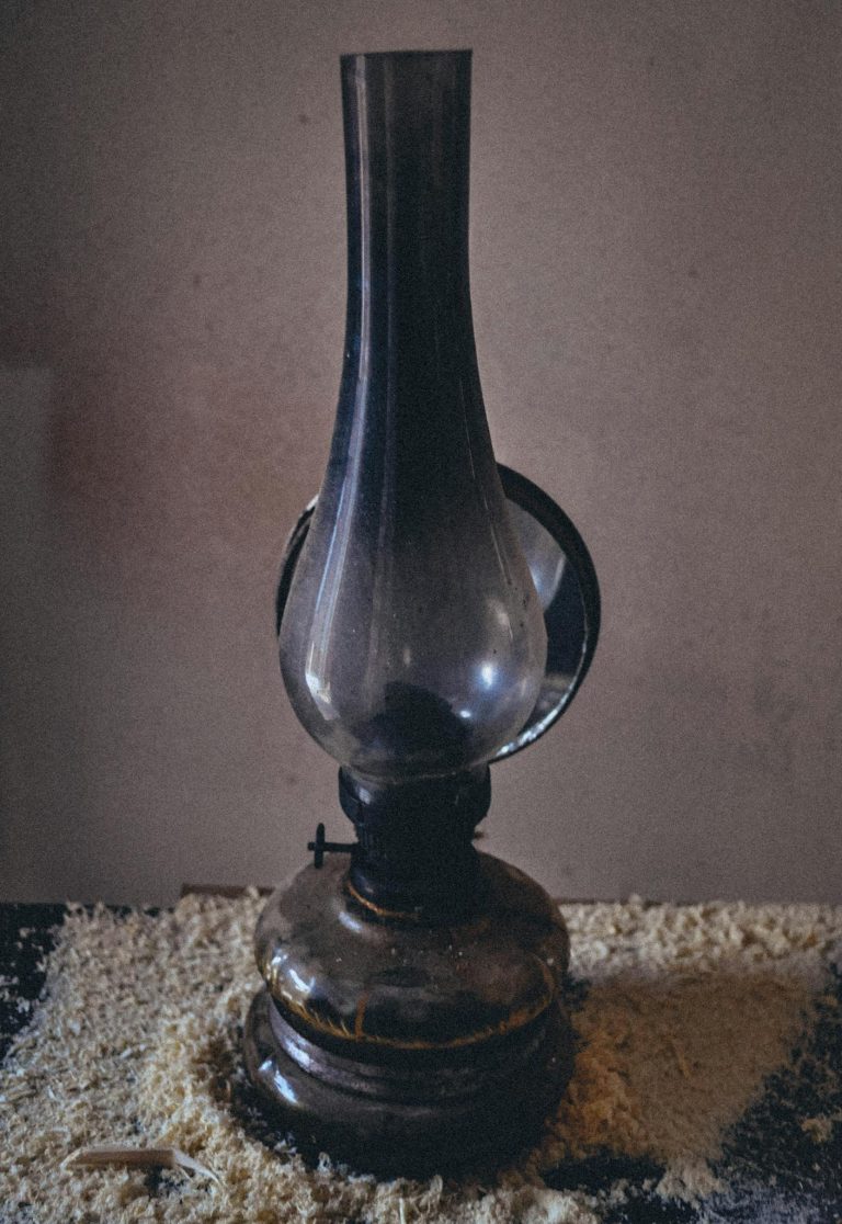 A dark, vintage glass oil lamp sits on a textured wooden table indoors.