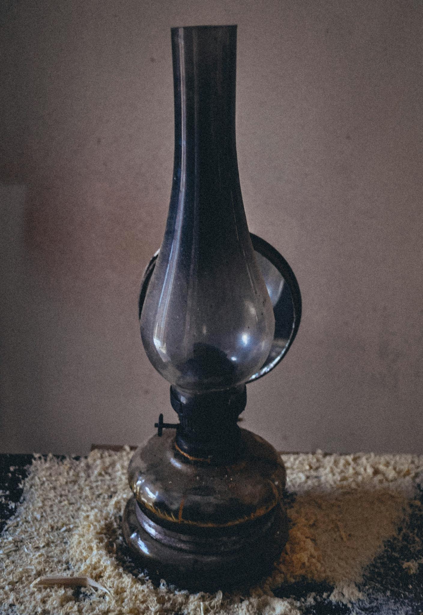 A dark, vintage glass oil lamp sits on a textured wooden table indoors.