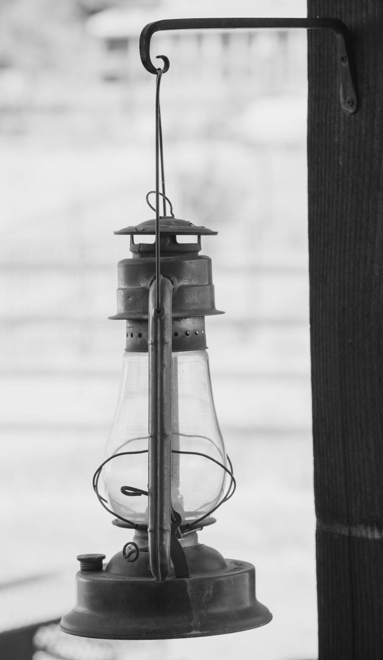 Black and white image of an antique kerosene lantern hanging on a wall.
