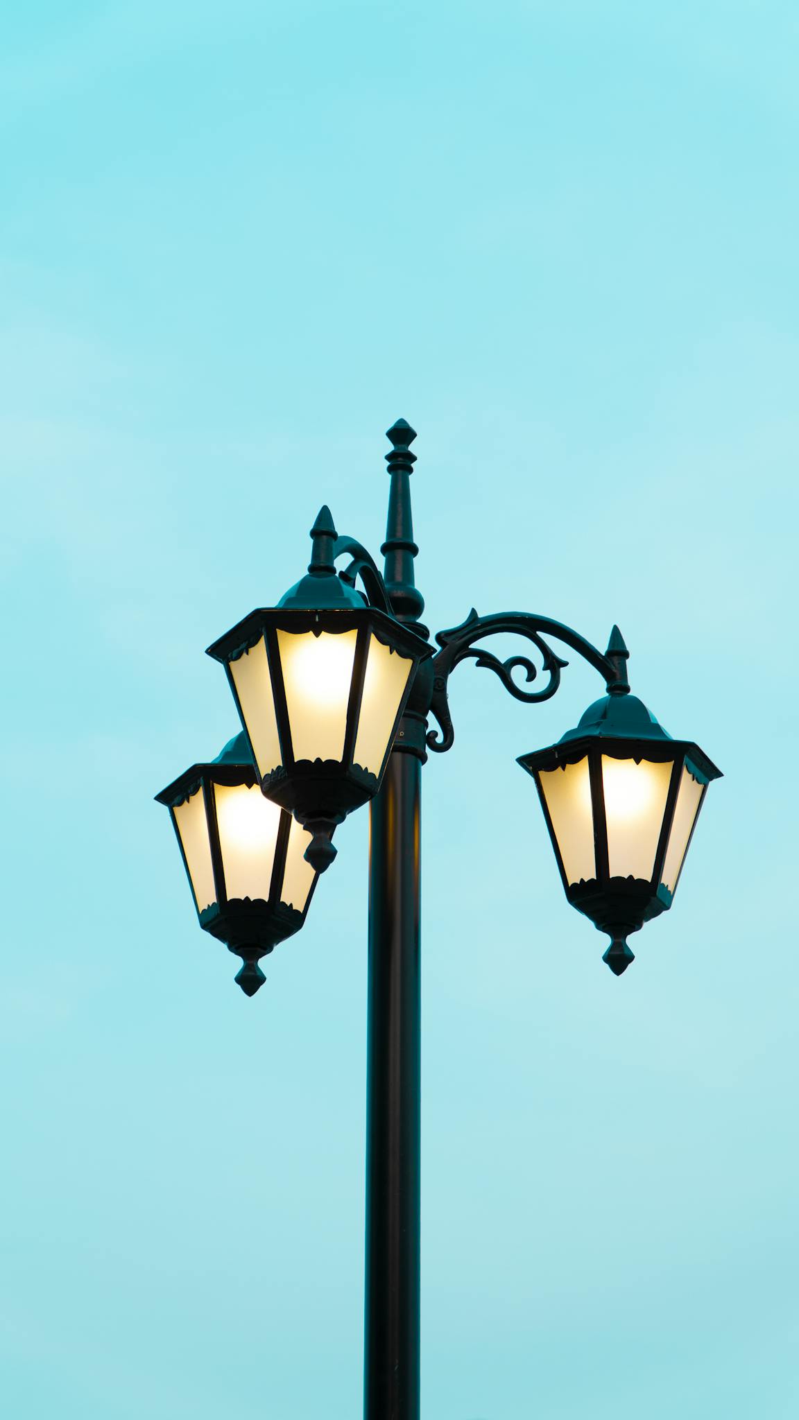 Classic vintage street lamp shining against a clear blue sky. Stylish urban decor.